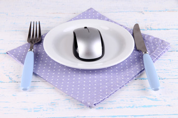 Computer mouse on plate with fork and knife on wooden