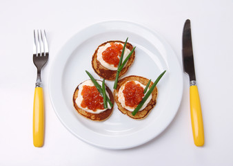 Pancakes with red caviar on plate, isolated on white