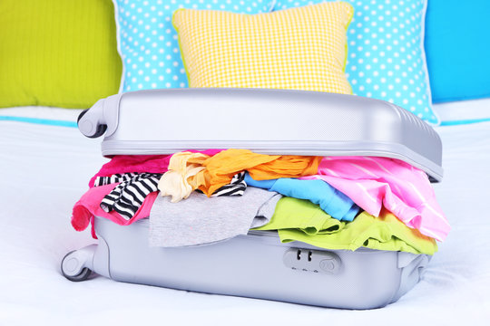 Grey suitcase with clothing on bed close-up