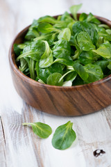 Vertical shot of a wooden bowl with fresh corn salad leaves