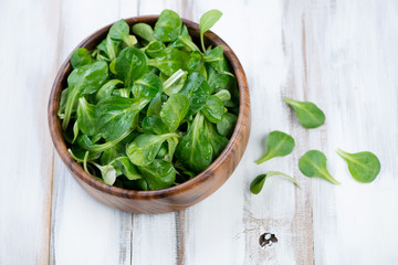 Wooden bowl with corn salad leaves, above view