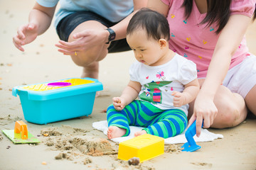 asian baby playing sand on the beach with father and mother