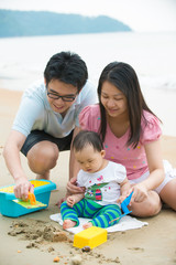 asian baby playing sand on the beach with father and mother
