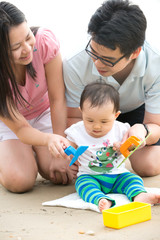 Obraz premium asian baby playing sand on the beach with father and mother