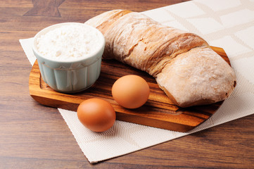 A bowl of flour, two eggs and a loaf of bread