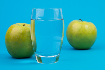 A glass with water and two green apples