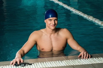 Muscular young man in blue cap in swimming pool
