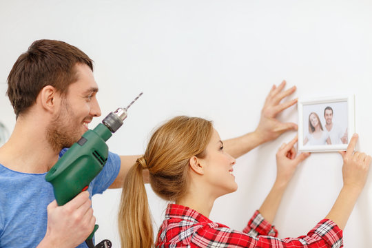 smiling couple drilling hole in wall at home