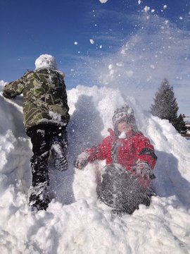snowball fight while two boys climb snow pile