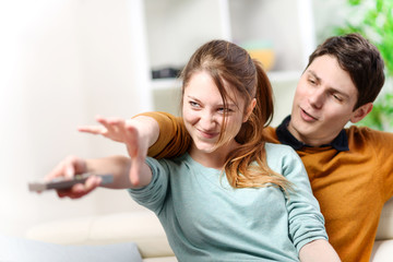 beautiful couple bickering to change tv channel on remote contro