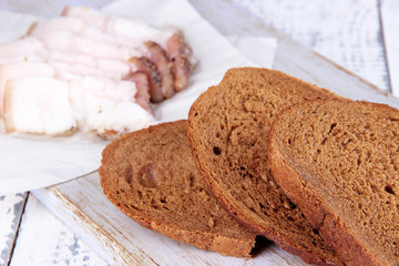 Slices of bread and lard on cutting board on wooden background