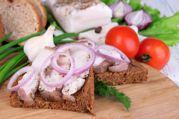 Slices of bread and lard with vegetables on table close up