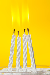 Burning white candles over yellow background