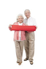 .Senior couple holding red streamer.