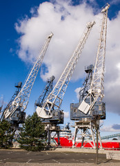 Horizontal color image of 3 old cranes in docks.