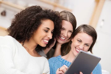 Fotobehang drei freundinnen schauen lachend auf tablet-pc © contrastwerkstatt