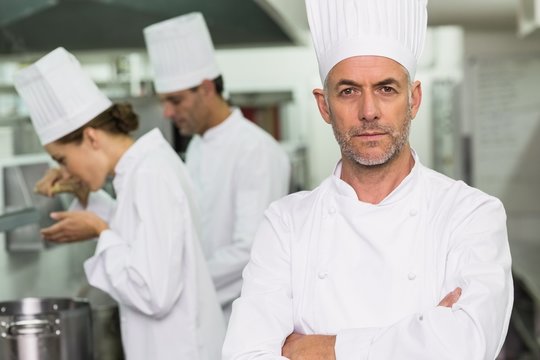 Serious chef looking at camera with team working behind