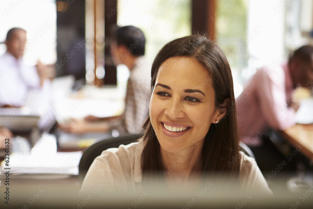 Wall mural businesswoman working at desk with meeting in background