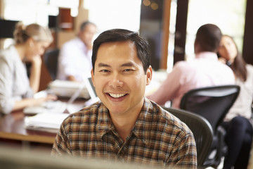 Businessman Working At Desk With Meeting In Background
