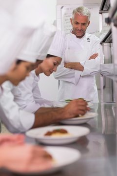 Head chef watching row of chefs garnishing spaghetti dishes
