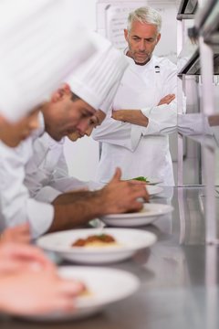 Head chef watching row of chefs garnishing spaghetti dishes with
