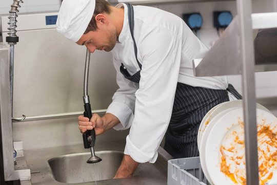Kitchen porter cleaning plates in sink
