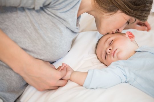 Mother kissing sleeping baby son on bed