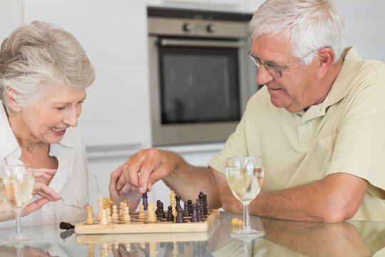 Smiling senior couple playing chess and having white wine
