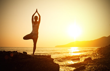 woman doing yoga on the beach at sunset