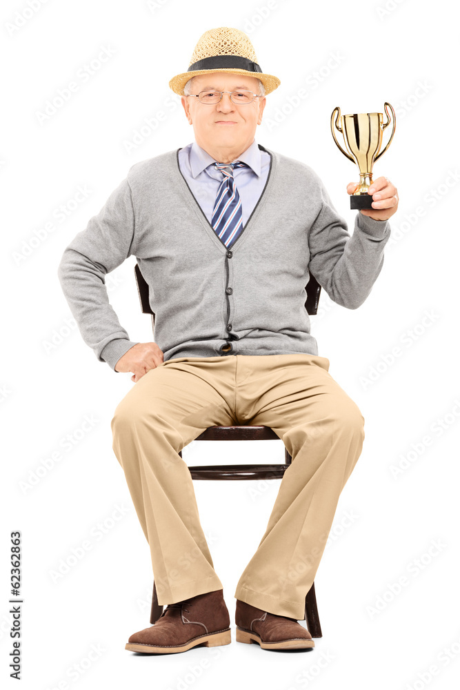 Wall mural Elderly gentleman sitting on a chair and holding a trophy