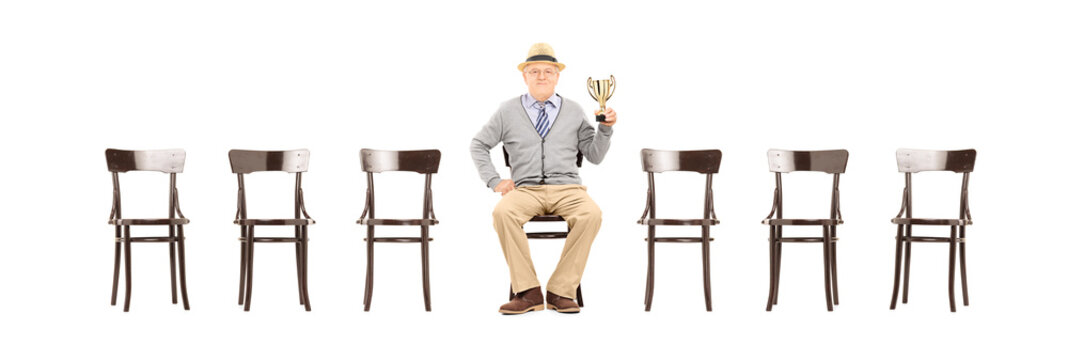 Mature man holding a trophy seated on wooden chair