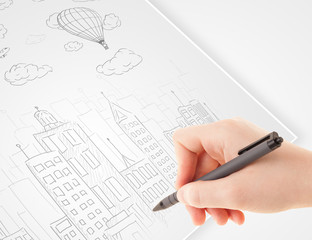 A person drawing sketch of a city with balloons and clouds on a