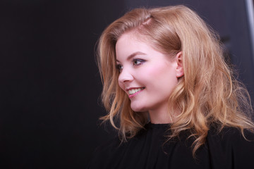Naklejka premium Smiling girl with blond wavy hair by hairdresser in beauty salon