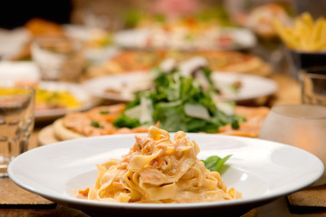 Table of pasta and other food plates in the background