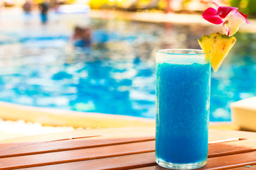 Tropical blue cocktail on woodem table near swimming pool