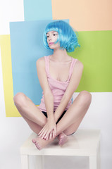 Funky Girl in Azure Wig Sitting in Studio on White Chair