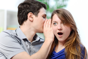 man whispering in the ear of his surprised wife