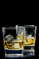 two glasses of alcoholic drink with ice on black background