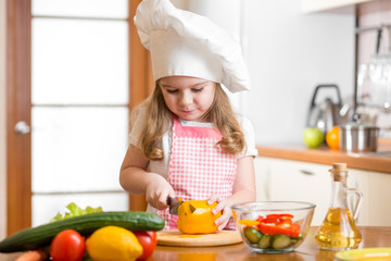Kid girl weared as cook cutting vegetables