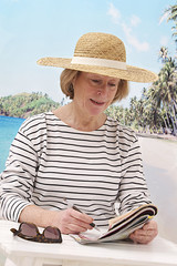relaxed woman with hat  sitting on beach doing crossword