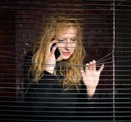Woman on the phone looking through venetian blinds