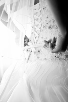 Black and white photo of bride tying corset on wedding dress