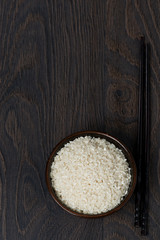 white rice in a bowl and chopsticks on dark background, top view