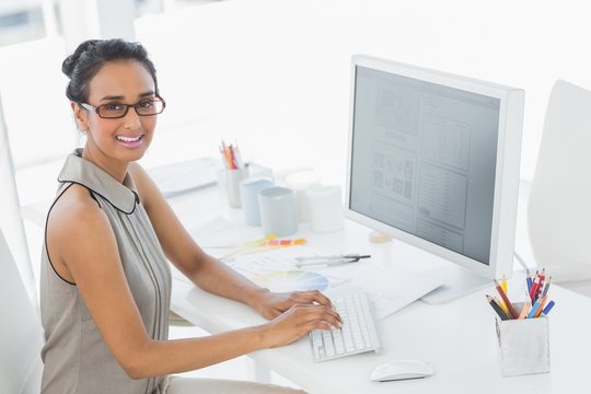 Designer working at her desk using computer smiling at camera