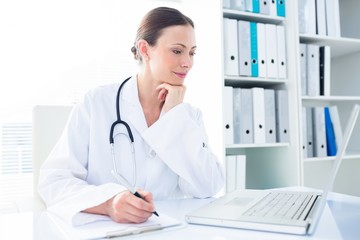 Doctor writing while using laptop