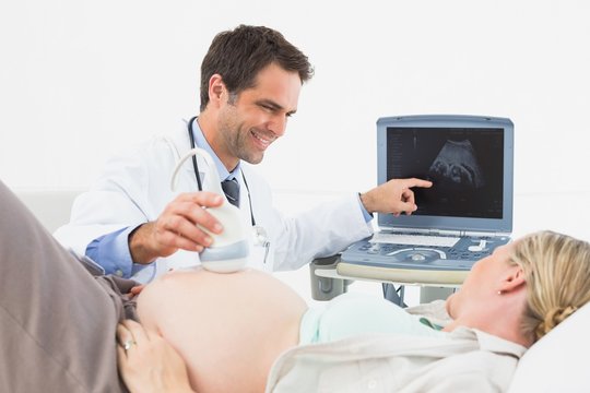 Happy doctor showing pregnant woman her baby on sonagram