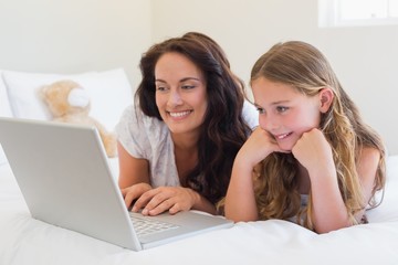 Mother and daughter using laptop in bed