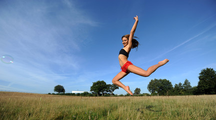 Frau in knappen sportsachen macht hohen  Sprung  vor blauem Himmel