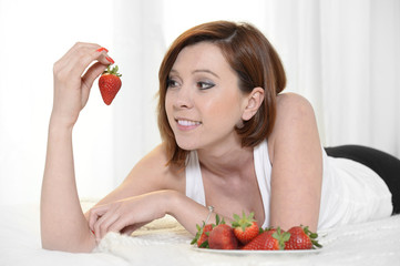 Young Attractive woman eating a bowl of strawberries in bed