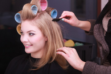 Blond girl hair curlers rollers by hairdresser in salon